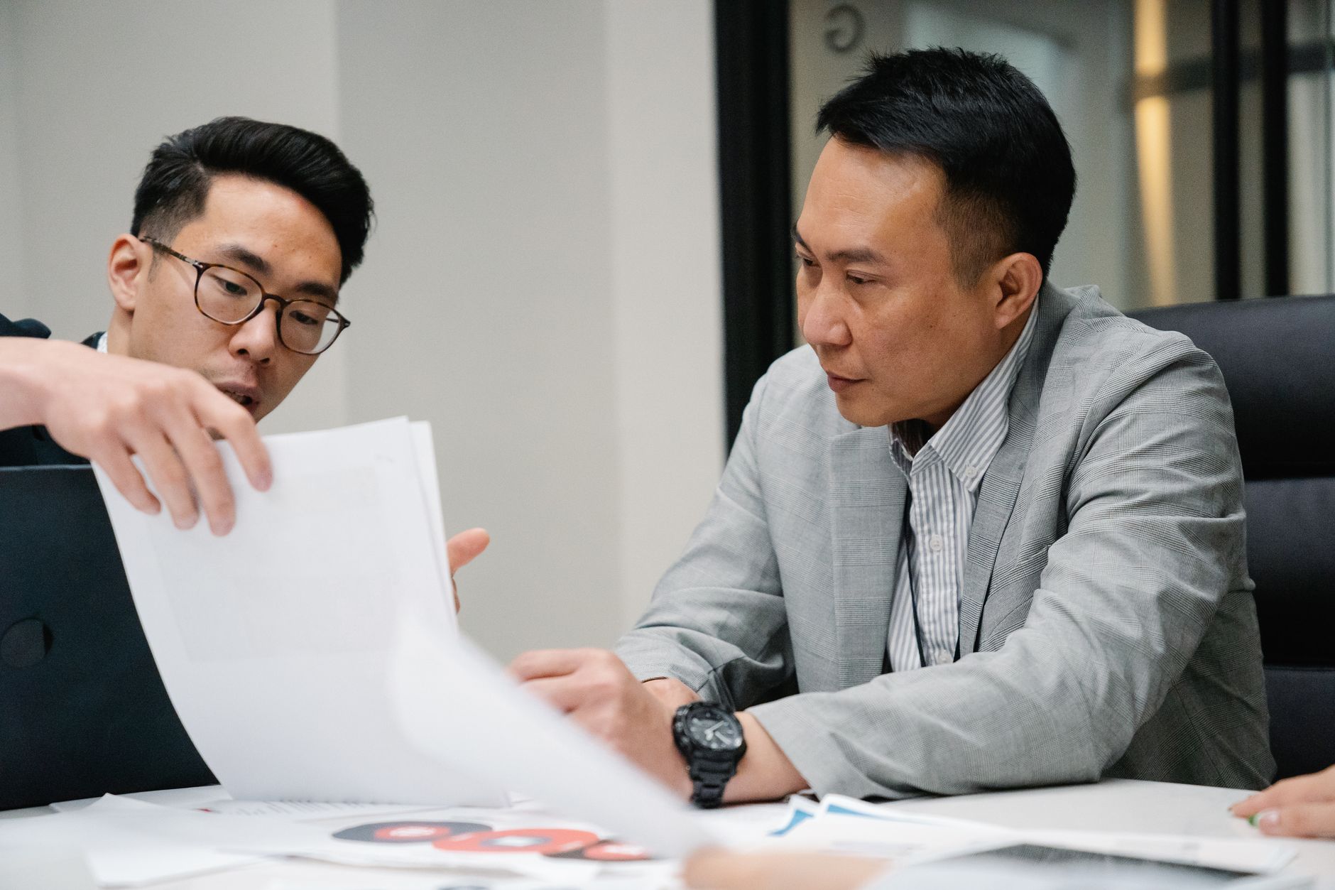 Two colleagues at a conference table review a printed report together, one pointing to a page